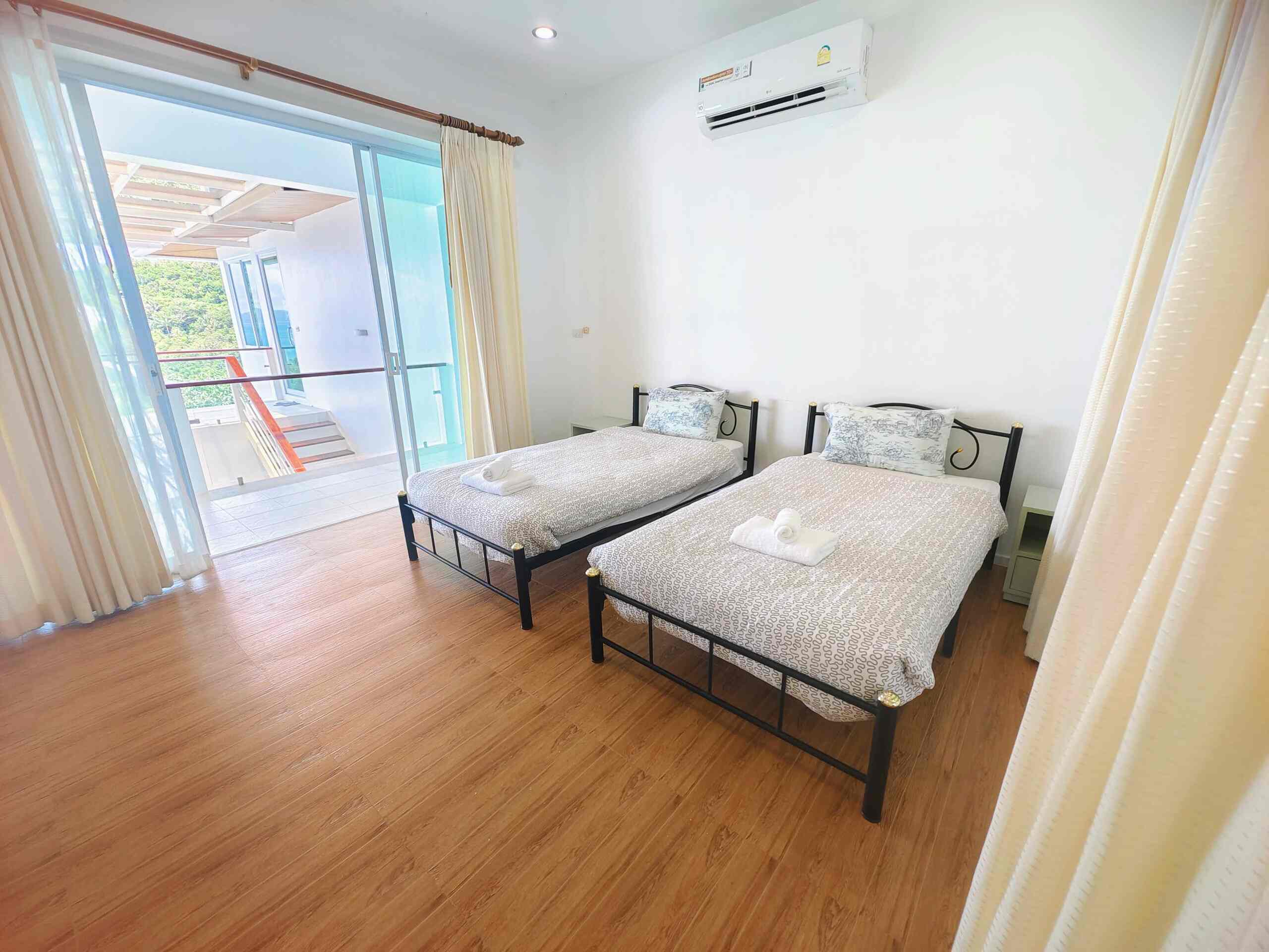 Bright bedroom with two twin beds, patterned bedding, rolled towels, wood floor, and glass door to balcony.