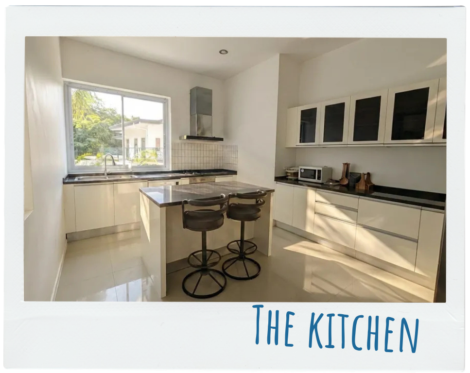 Bright modern kitchen with a window, island with stools, black countertops, and white cabinets.